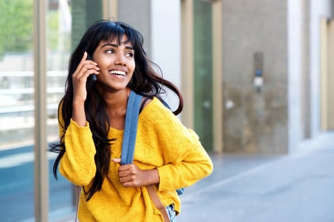 Portrait of happy young Indian woman walking with mobile phone and bag