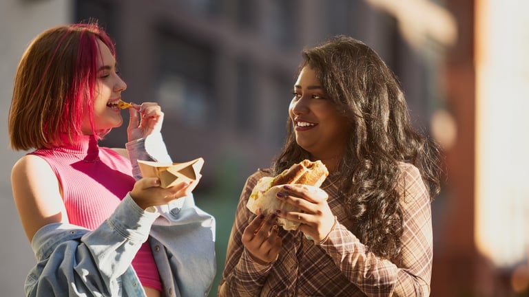 Two girls smiling and sharing fries and sandwich in bright daylight